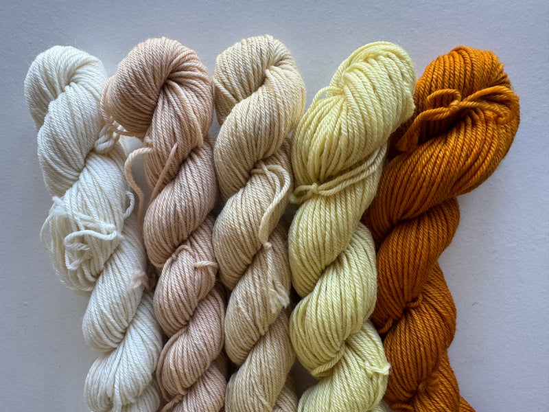 Five skeins of yarn in white, beige, yellow, and orange on a light gray background