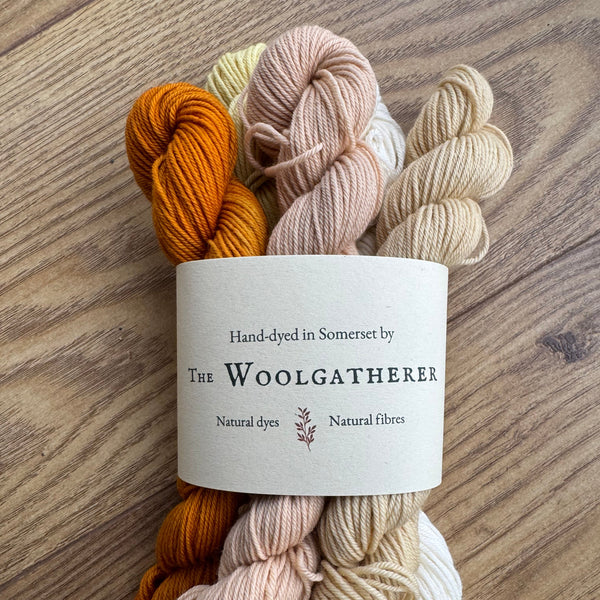 Yarn skeins in beige, orange, and white with a label on a wooden surface